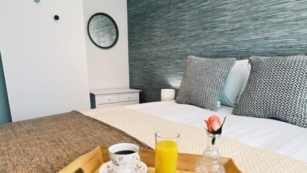 Et hotelværelse med en seng, et natbord, et bakke med morgenmadsprodukter og en væg med et struktureret design.