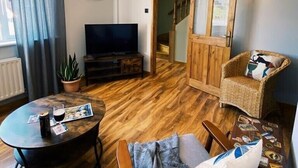 En hyggelig stue med trægulv, et rundt sofabord, en sofa, et fjernsyn og en trappe til et andet rum.
