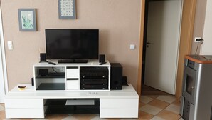 Een woonkamer met een flatscreen televisie op een witte dressoir, een speaker en een lijst met een afbeelding aan de muur.