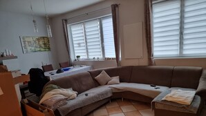 Een woonkamer met een modulaire bank, een eettafel en een schilderij aan de muur.