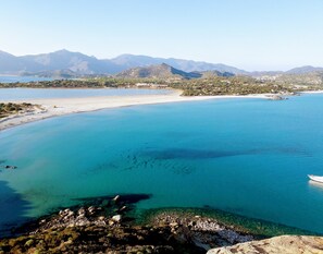 A coastal landscape with clear turquoise waters, a sandy beach, and distant mountains. - Appartamento vacanza presso Teatro Lirico Cagliari (Cagliari)
