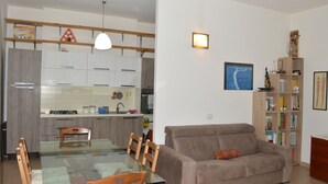Ett modernt kök med vita skåp, ett matbord med stolar, en soffa och en bokhylla.