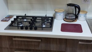 Ett kök med en gasspis, två behållare i rostfritt stål, en kaffebryggare och en röd skärbräda.