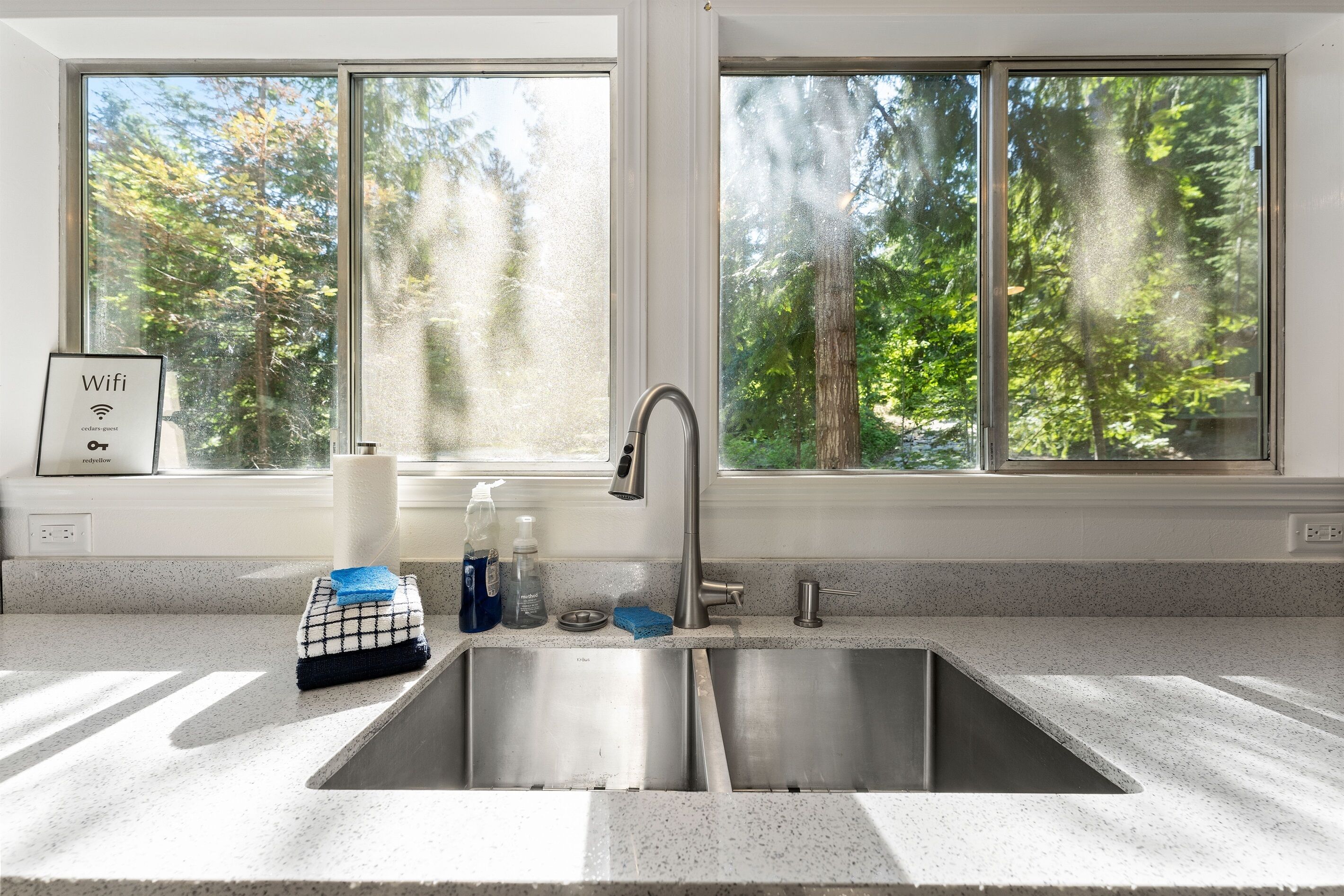 Una cocina con un lavamanos de acero inoxidable, una ventana con vistas a árboles y un letrero que indica disponibilidad de wifi.