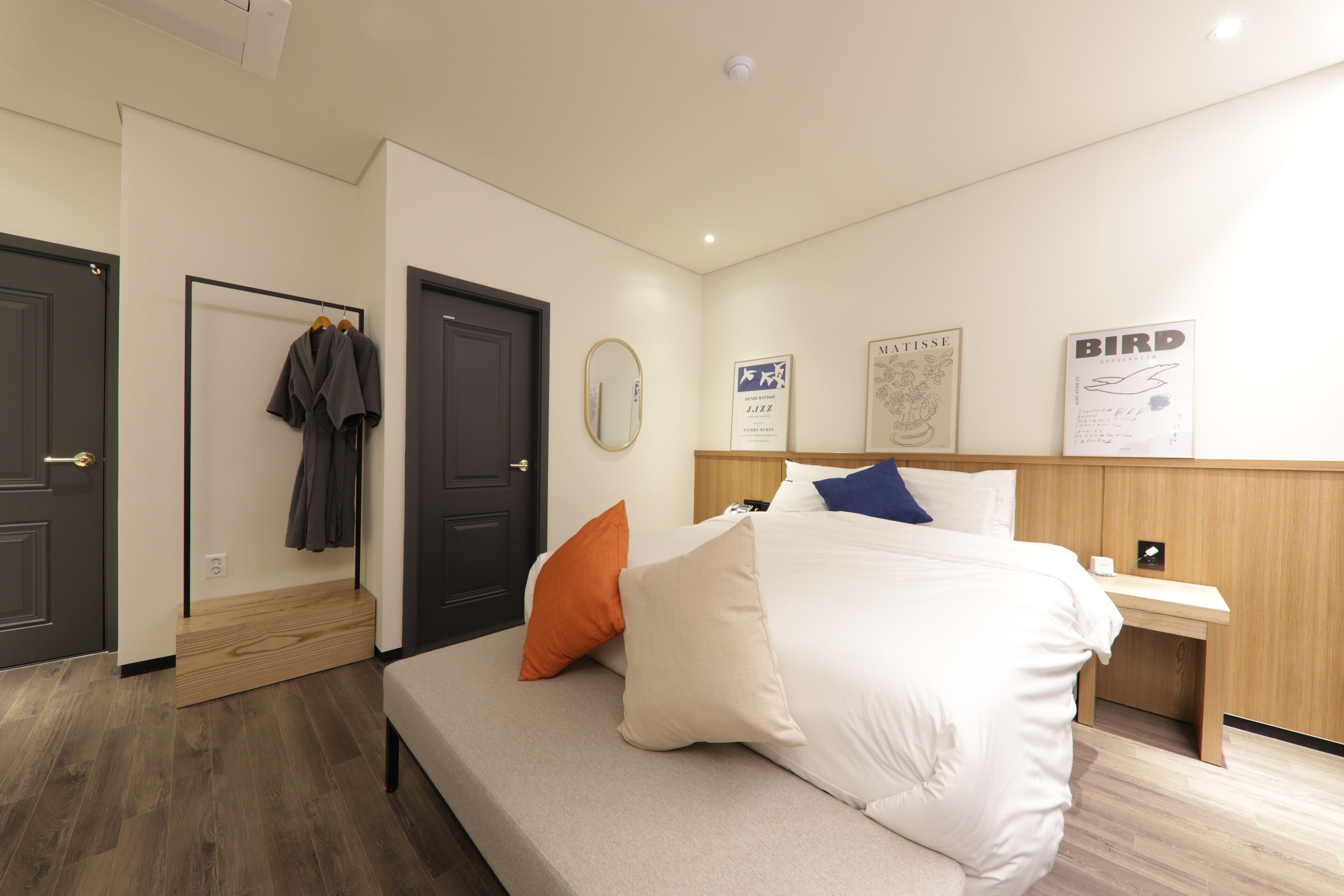 A hotel room with a bed, a bench, a wooden nightstand, and a wall with framed artwork.
