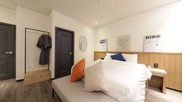 A hotel room with a bed, a bench, a wooden nightstand, and a wall with framed artwork.
