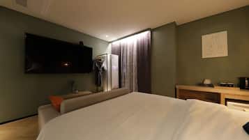 A modern hotel room with a large bed, a flat-screen TV mounted on the wall, a desk with a coffee maker, and a painting on the wall.