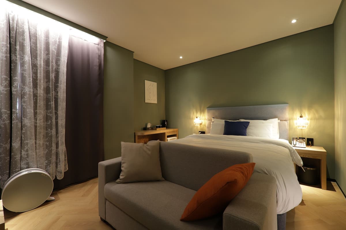 A modern hotel room with a bed, a sofa, and a bedside table.