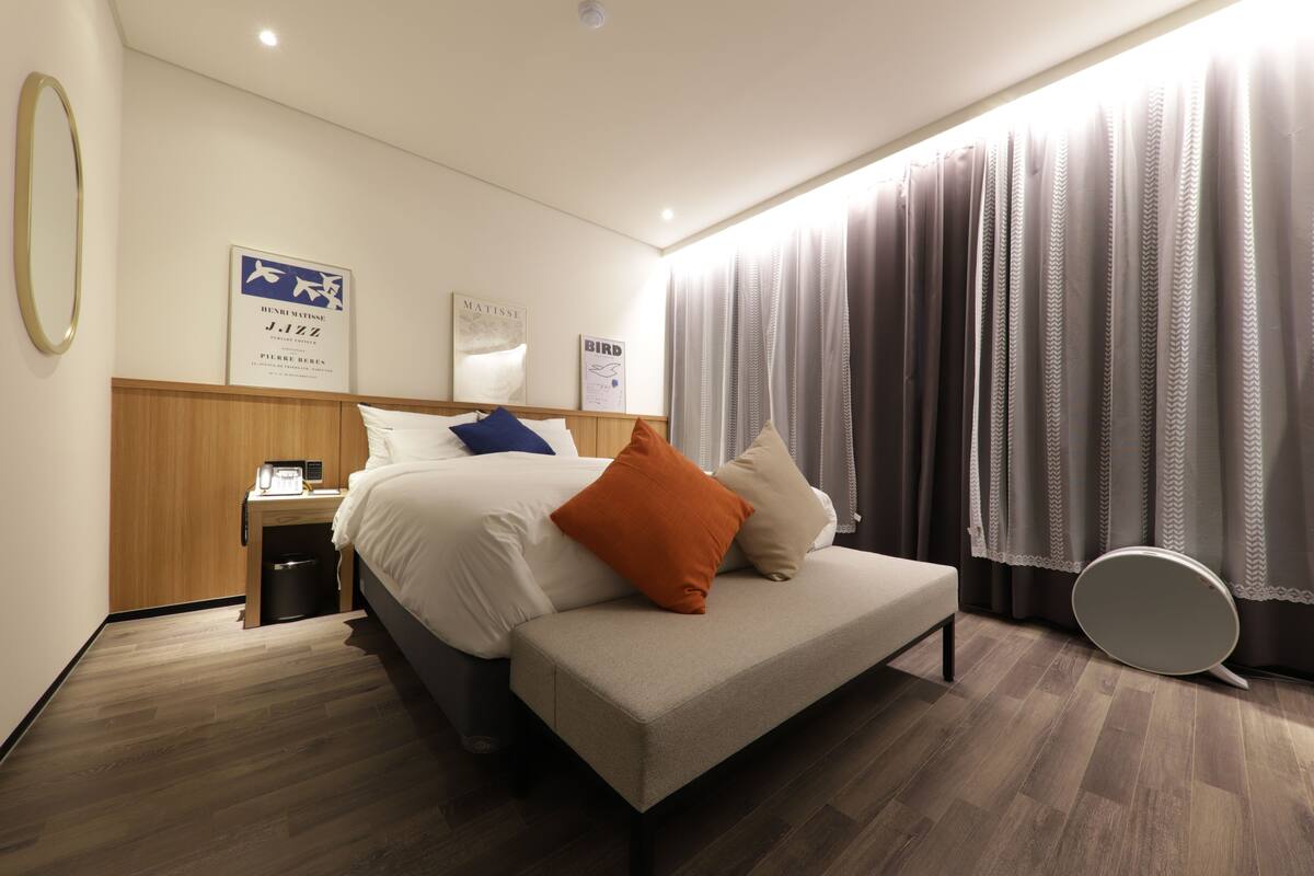 A modern hotel room with a bed, nightstand, and a large window with curtains.