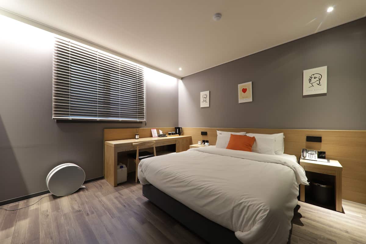 A modern hotel room with a large bed, a desk, and a small bedside table.