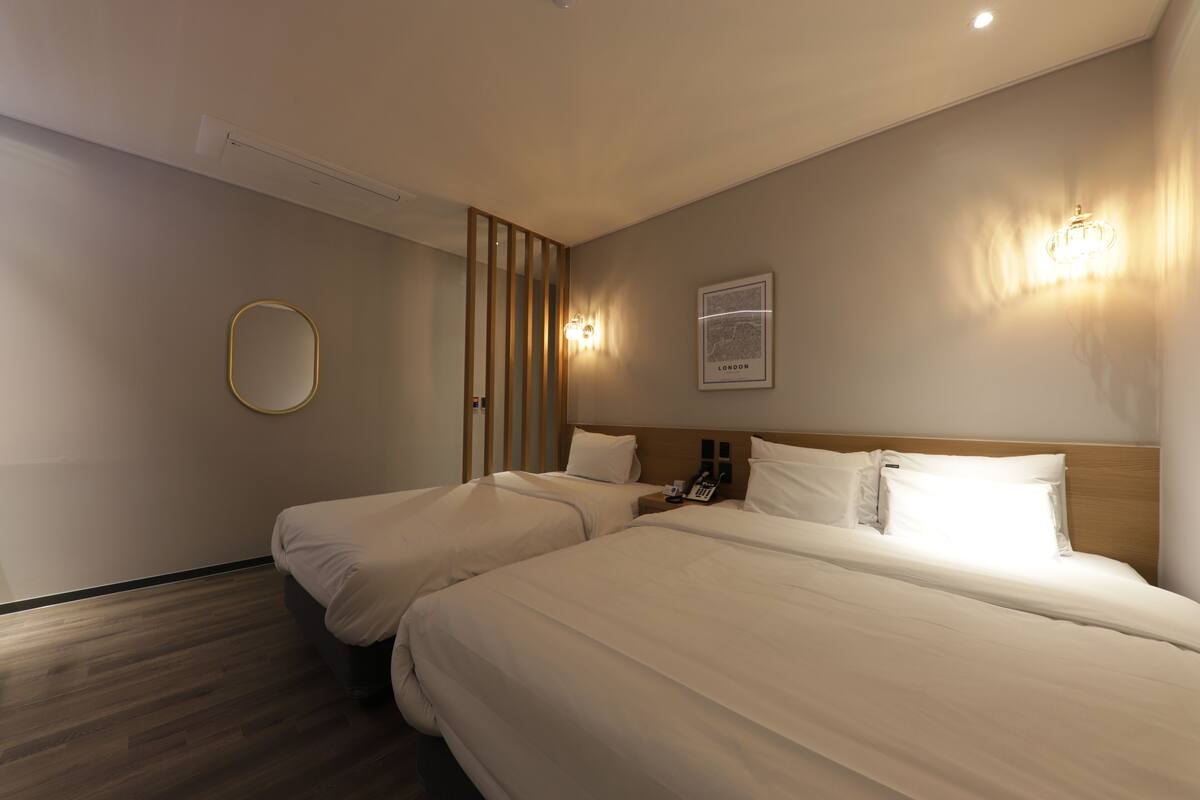 A hotel room with two beds, a wooden headboard, a bedside table with a phone, and a wall-mounted light fixture.