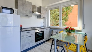 Una cocina moderna con microondas integrado, horno y estufa a gas. Hay una mesa de vidrio con sillas amarillas y una cesta de flores encima.