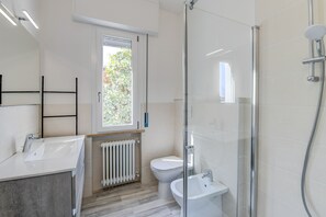 A modern bathroom with a glass shower enclosure, a white sink, a toilet, and a window providing natural light.