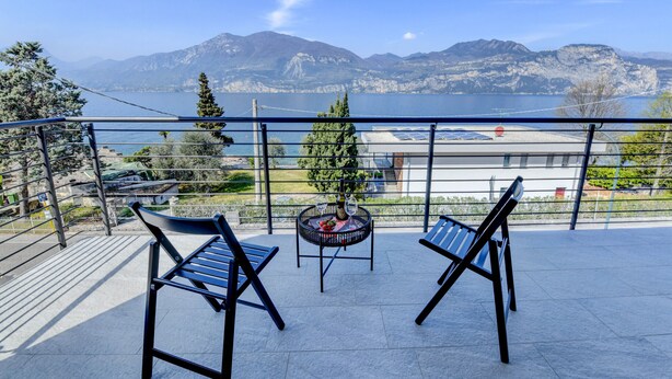 Un balcon avec deux chaises et une petite table, d’où l’on peut admirer un lac et des montagnes.