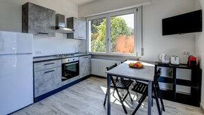 Une cuisine moderne dotée d’un four encastré, d’une table à manger avec des chaises et d’une grande fenêtre donnant sur un paysage verdoyant.