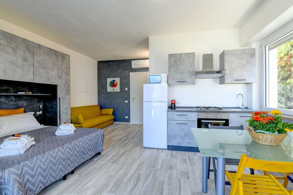 A compact hotel room with a bed, a sofa, a kitchenette, and a dining area.