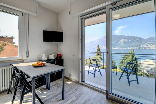 Una habitación moderna con una mesa de comedor, sillas, un televisor de pantalla plana y un ventanal corredera que da a un balcón con vistas a montañas y una masa de agua.