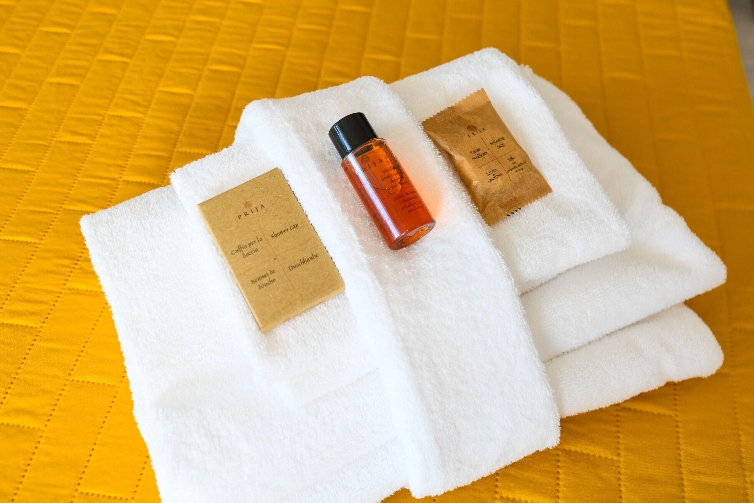 A white towel with a bottle and a brown tag on a yellow quilted bedspread.