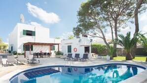 A swimming pool with lounge chairs and a patio area, surrounded by white buildings and trees. - Spacious holiday home Dos Pinos with pool, A/C 24h, Wi-Fi, near Cala Esmeralda (Santanyí)