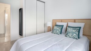 Une chambre à coucher comprenant un lit, une armoire, une lampe de chevet et une tête de lit en rotin.