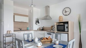 A modern kitchen with white cabinets, a microwave, a toaster, and a coffee machine. There is a dining table with chairs and a vase of flowers. - 50m from the beach, seaview flat for 2 (Pléneuf-Val-André)