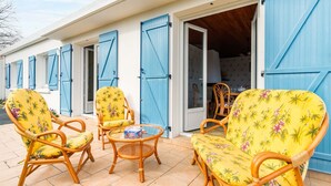 A covered outdoor seating area with wicker chairs and a table, adjacent to a building with blue shutters. - Holiday home for 6 in Saint Hilaire de Riez (Saint-Hilaire-de-Riez)
