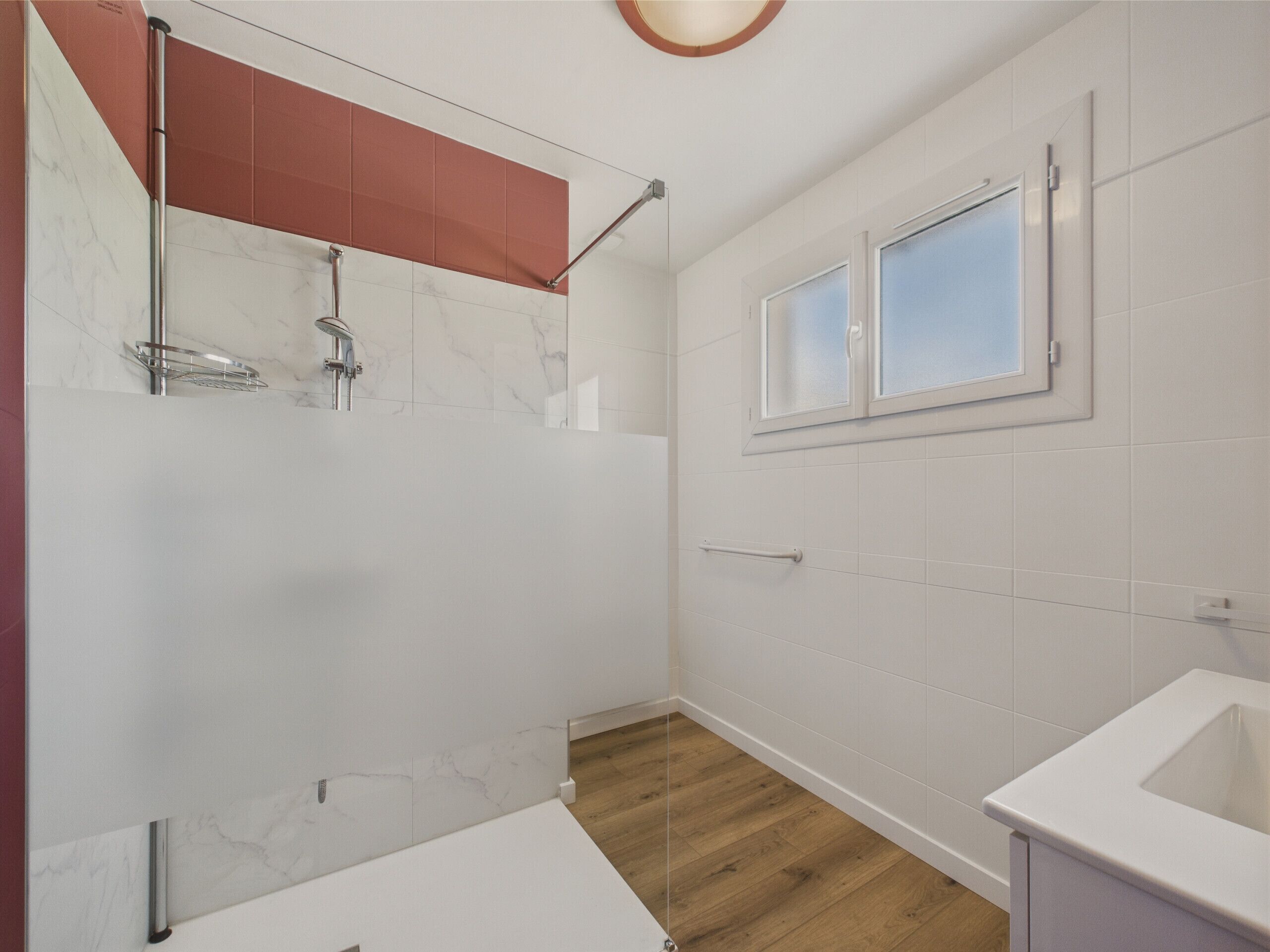 A bathroom with a shower, a window, and a sink.