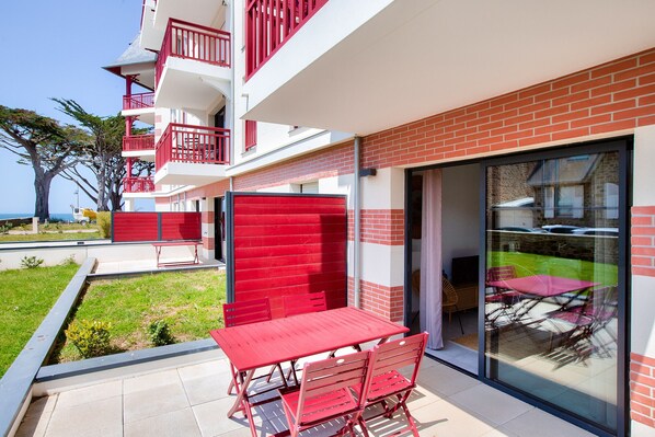A modern building with a red and white color scheme, featuring a balcony with red railings and a glass door leading to an outdoor seating area. - 50m from the beach, lovely flat for 4 (Pléneuf-Val-André)