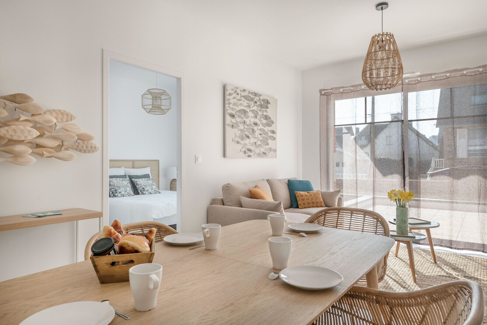 A modern, well-lit room with a dining table set for two, a sofa, and a large window with a view.