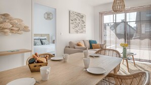 Una habitación moderna y luminosa con una mesa de comedor preparada para dos personas, un sofá y un ventanal con vistas.