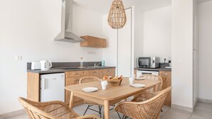 Una cocina moderna con comedor, que incluye una mesa de madera, sillas de mimbre y una lámpara colgante.