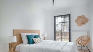 Ein Schlafzimmer mit einem großen Bett, zwei Nachttischen mit Lampen, einem Fenster mit Vorhängen, einem Rattan-Sessel und einem Wanddekor.