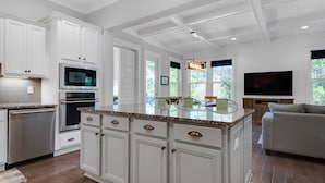 Une cuisine moderne avec des meubles blancs, un four encastré et un grand îlot central doté d’un plan de travail en verre.