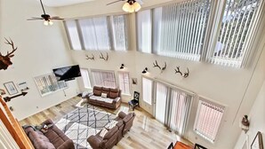A spacious living area with a high ceiling, large windows, a ceiling fan, and a flat-screen TV. - Cascade Cabin Mountain Getaway with Private Beach (Cascade)