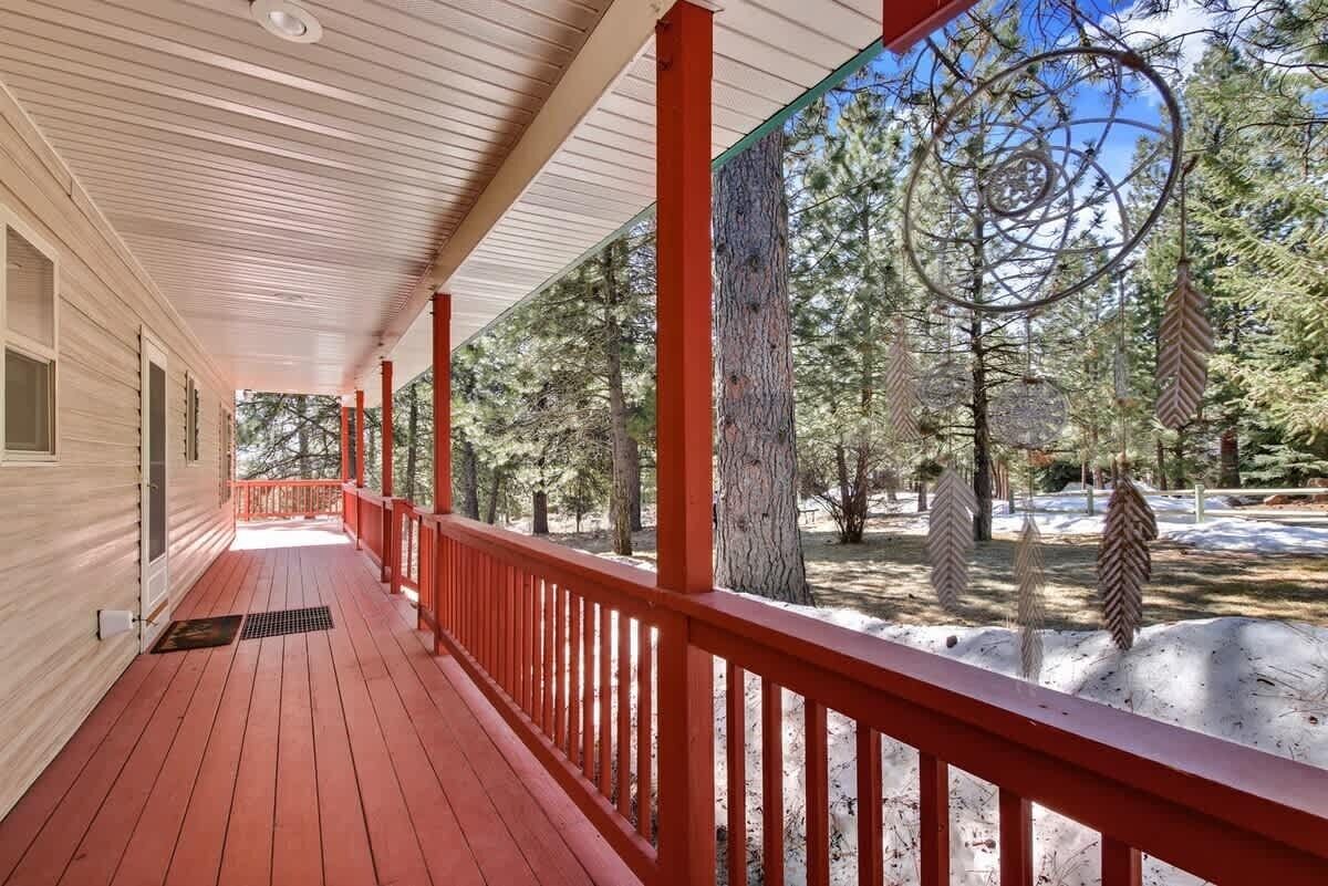Eine überdachte Veranda mit roten Geländern, einem Holzboden und Blick auf eine verschneite Landschaft mit Bäumen.