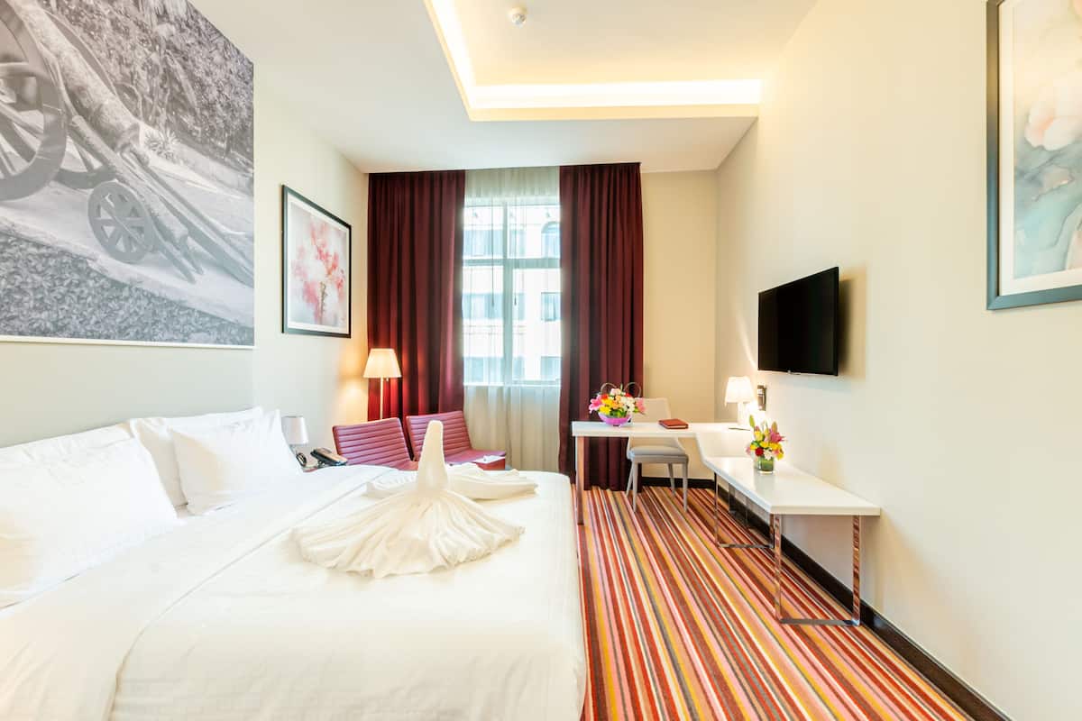 A hotel room with a large bed, a desk, a chair, a TV, and a window with curtains.