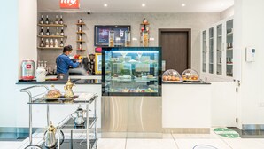 A modern cafe with a glass display case, shelves with beverages, and a digital menu board. - Gravity Hotel (Abu Dhabi)
