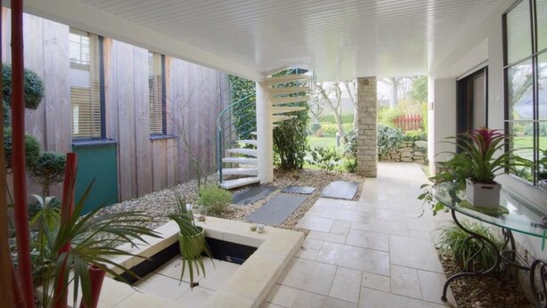 A modern outdoor patio with a spiral staircase, stone pillars, and potted plants. - 4-star house with patio and garden (Arradon)