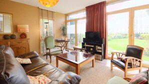 A living room with a leather sofa, a coffee table, a television, and a large window with curtains. - 4-star house with patio and garden (Arradon)