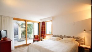 A bedroom with a large bed, a TV on a stand, a chair, a lamp, and a view of a staircase and greenery outside. - 4-star house with patio and garden (Arradon)