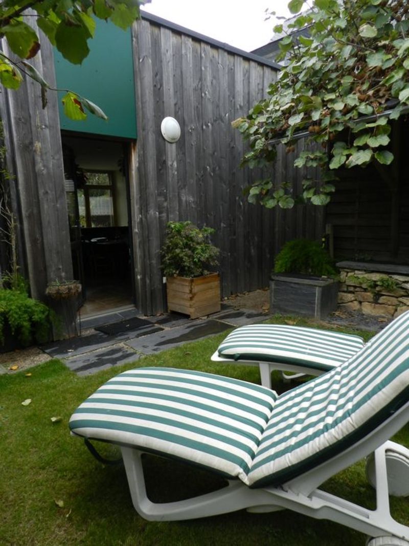 A backyard with two striped lounge chairs, a wooden fence, and a small garden area.