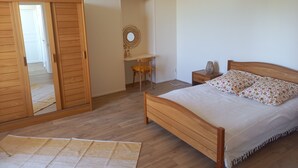 Een slaapkamer met een houten bed, een bureau, een stoel, een nachtkastje, een spiegel en een kledingkast.