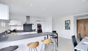 A modern kitchen with a central island, bar stools, and a dining table with chairs. - Les Thoniers - Etel - Gîte (ETEL)