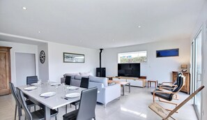 A modern living room with a dining area, a sofa, a TV, and a fireplace. - Les Thoniers - Etel - Gîte (ETEL)