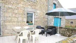 A stone building with a tiled patio, outdoor seating, and a blue door. - Les Saules Blancs - Plouharnel (PLOUHARNEL)