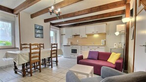 A cozy living room with a dining table, wooden chairs, a sofa, and a kitchen in the background. - Les Saules Blancs - Plouharnel (PLOUHARNEL)