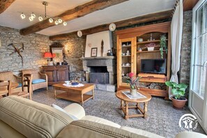 A cozy living room with a stone wall, wooden furniture, a fireplace, and a television. - Pont Bihan - CARNAC - Gîte (CARNAC)