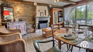 A rustic interior with stone walls, a fireplace, wooden furniture, and a dining area with a view of greenery outside. - Pont Bihan - CARNAC - Gîte (CARNAC)