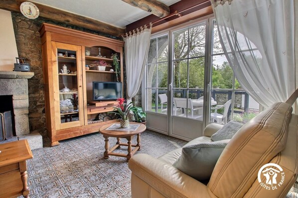 A cozy living room with a fireplace, wooden cabinet, TV, and a large window with curtains.