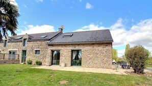 A stone house with a sloped roof, large windows, and a paved driveway.